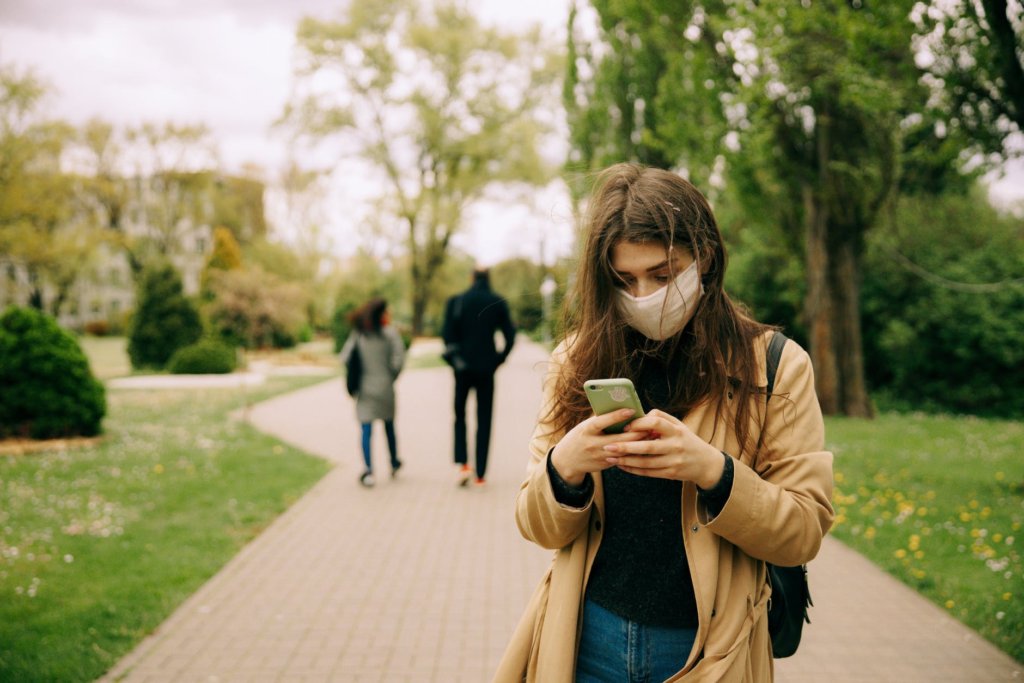 Student on facemask using phone on a school path